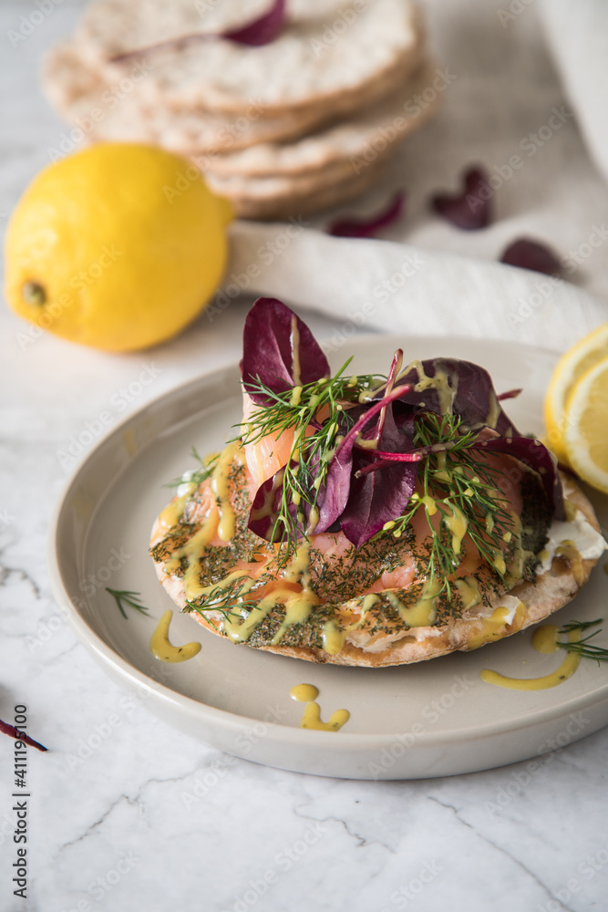 Gravlax Graved Lachs auf Knäckebrot mit Rote Beete Blätter Salat, Dill, Fischkäse, Skandinavische Senf Soße, Zitrone auf hell Marmor Hintergrund mit Leinen Tuch als Vorspeise oder Snack