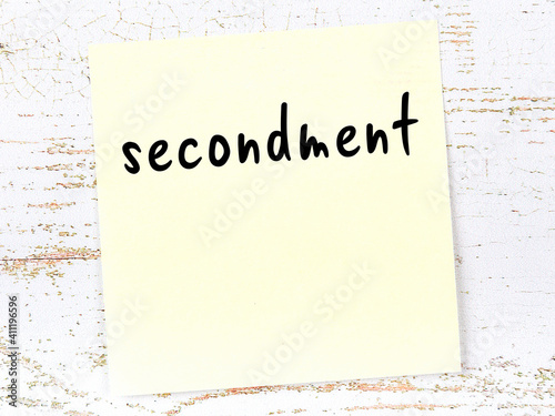 Yellow sticky note on wooden wall with handwritten word secondment photo