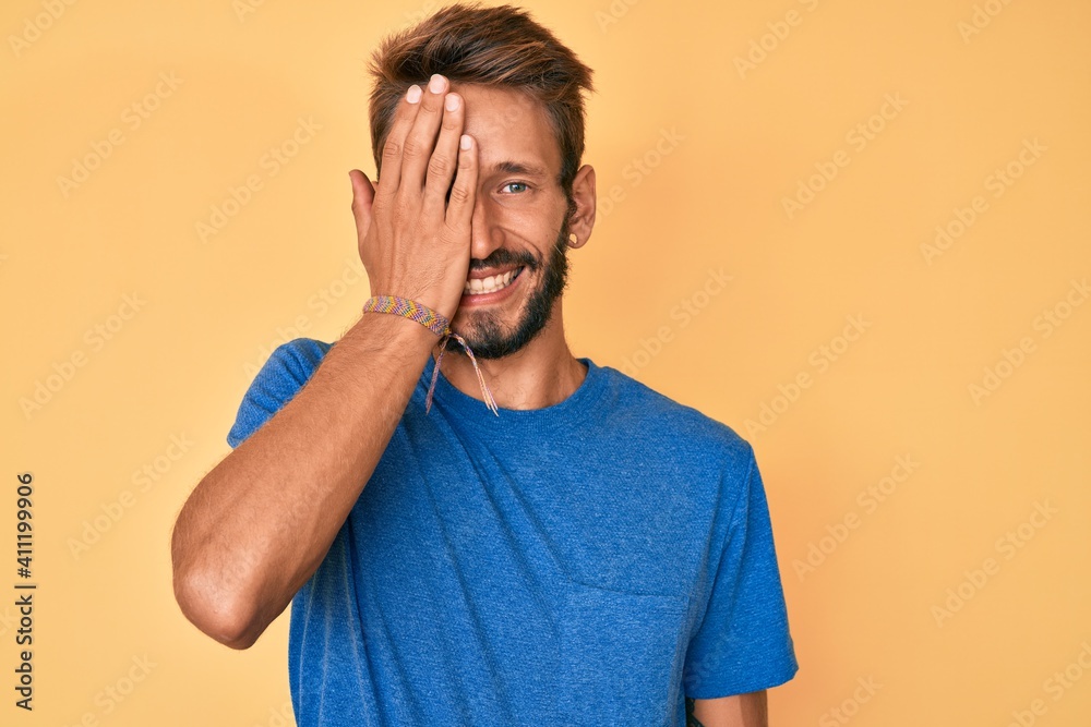 Handsome caucasian man with beard wearing casual clothes covering one eye with hand, confident smile on face and surprise emotion. Handsome caucasian man with beard wearing casual clothes covering one eye with hand, confident smile on face and surprise emotion.