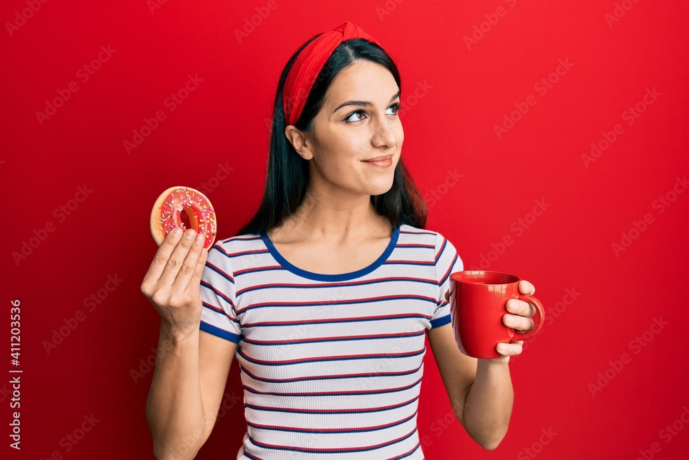 Young hispanic woman eating doughnut and drinking coffee smiling looking to the side and staring away thinking. Young hispanic woman eating doughnut and drinking coffee smiling looking to the side and staring away thinking.