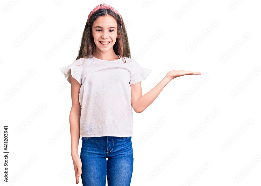Cute hispanic child girl wearing casual white tshirt smiling cheerful presenting and pointing with palm of hand looking at the camera. Cute hispanic child girl wearing casual white tshirt smiling cheerful presenting and pointing with palm of hand looking at the camera.