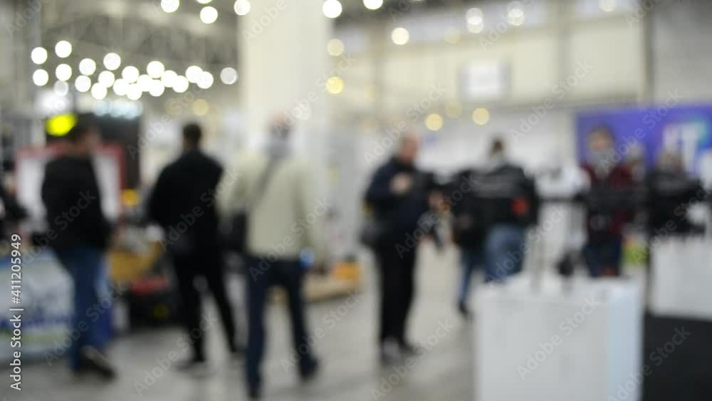 Blurred background. People walk inside large space building. Exhibition presentation. Abstract background and bokeh spots with moving people indoors. Hall, lobby, entry. People walk inside space. Blurred background. People walk inside large space building. Exhibition presentation. Abstract background and bokeh spots with moving people indoors. Hall, lobby, entry. People walk inside space.