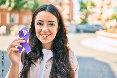 Фотография Young hispanic woman smiling happy holding purple ribbon walking at the city