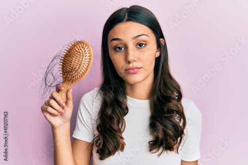 Young hispanic woman styling hair using comb thinking attitude and sober expression looking self confident photo