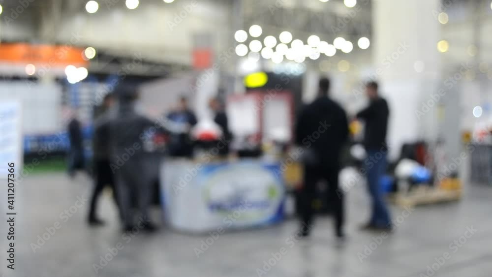 Blurred background. People walk inside large space building. Exhibition presentation. Abstract background and bokeh spots with moving people indoors. Hall, lobby, entry. People walk inside space. Blurred background. People walk inside large space building. Exhibition presentation. Abstract background and bokeh spots with moving people indoors. Hall, lobby, entry. People walk inside space.