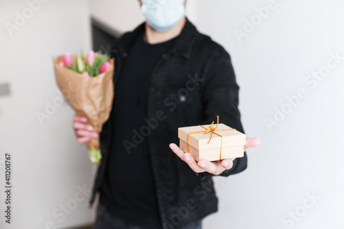A man in medical mask delivering a gift box and a craft bouquet during the pandemic 
