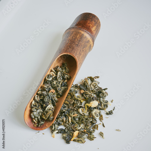 Chinese green jasmine tea with jasmine dry flowers in the wooden tea spoon on white background