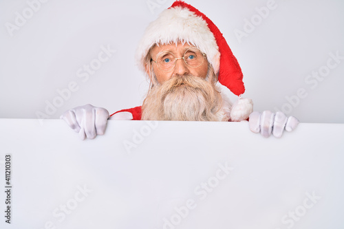 Old senior man with grey hair and long beard wearing santa claus costume holding banner relaxed with serious expression on face. simple and natural looking at the camera.