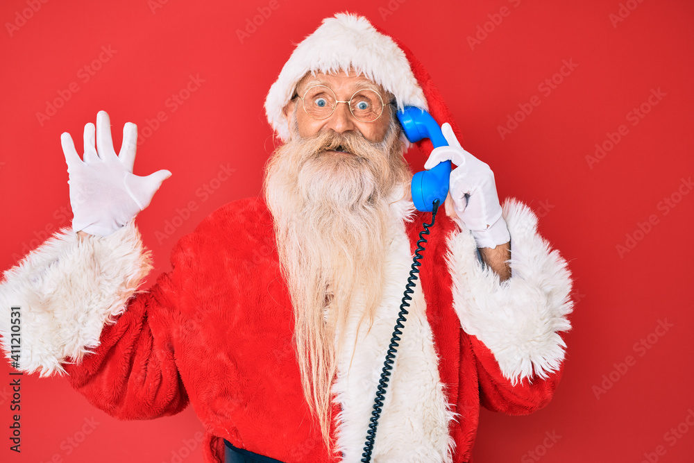 Old senior man wearing santa claus costume using vintage telephone celebrating victory with happy smile and winner expression with raised hands Old senior man wearing santa claus costume using vintage telephone celebrating victory with happy smile and winner expression with raised hands