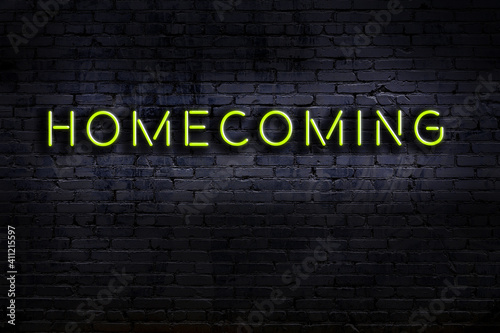 Night view of neon sign on brick wall with inscription homecoming photo