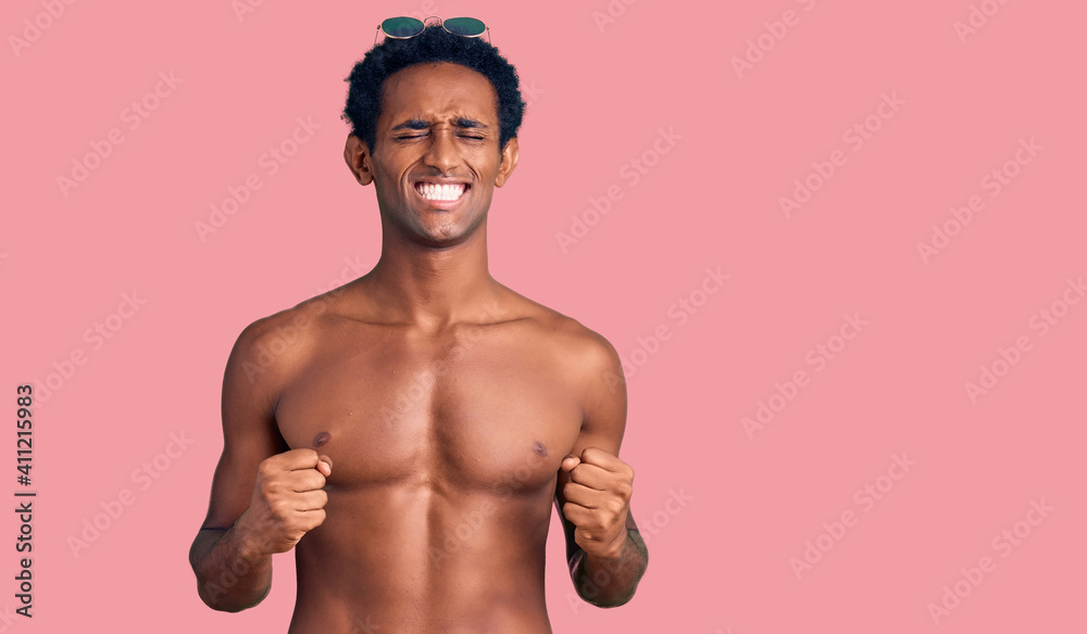 Fototapeta premium African handsome man wearing swimsuit and sunglasses excited for success with arms raised and eyes closed celebrating victory smiling. winner concept.