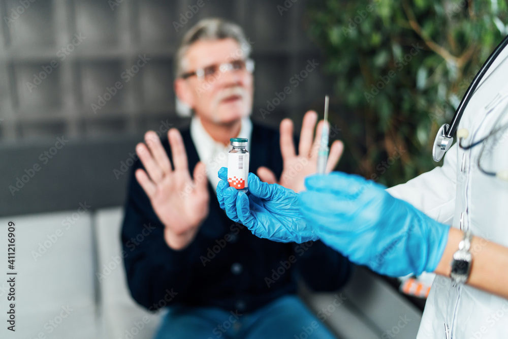 Close up of a nurse's hand in blue protective gloves holding an ampoule with the vaccine and a prick in his hands, on the background a blurred man who is saying the vaccine. Vaccine against covid-19. 
