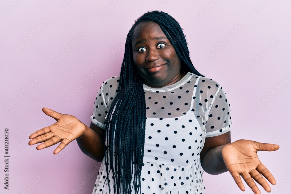 Young black woman with braids wearing casual clothes clueless and confused expression with arms and hands raised. doubt concept. Young black woman with braids wearing casual clothes clueless and confused expression with arms and hands raised. doubt concept.