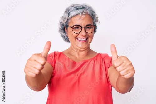 Senior hispanic grey- haired woman wearing casual clothes and glasses approving doing positive gesture with hand, thumbs up smiling and happy for success. winner gesture.