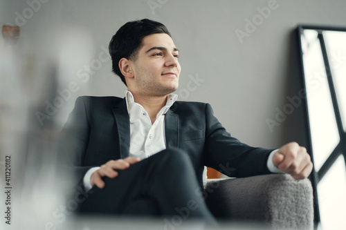 a confident economist, a dark-haired man of European appearance in a business suit. he smiles and looks away. works sitting in a new stylish office on the couch. senior manager