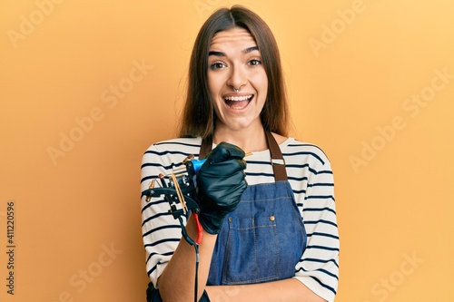 Young hispanic woman tattoo artist wearing professional uniform and gloves celebrating crazy and amazed for success with open eyes screaming excited.