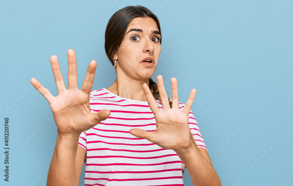 Young hispanic woman wearing casual clothes afraid and terrified with fear expression stop gesture with hands, shouting in shock. panic concept. Young hispanic woman wearing casual clothes afraid and terrified with fear expression stop gesture with hands, shouting in shock. panic concept.