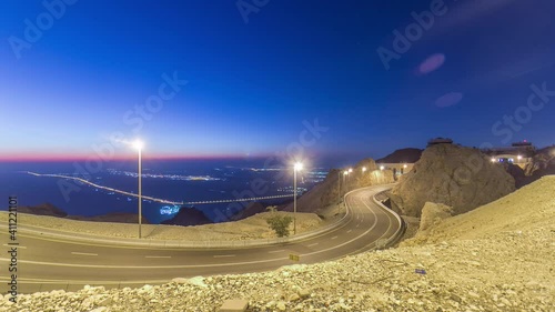 Day to night transition timelapse with rocks and Curvy road on Jebel Hafeet. Mountain located primarily in the environs of Al Ain and offers an impressive view over the city. Aerial view from top photo