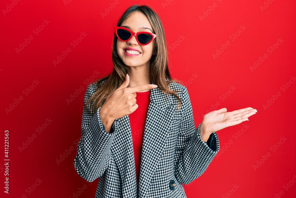 Young brunette woman wearing fashion and modern look amazed and smiling to the camera while presenting with hand and pointing with finger. Young brunette woman wearing fashion and modern look amazed and smiling to the camera while presenting with hand and pointing with finger.