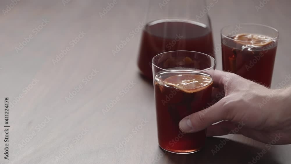 Slow motion man hand take mulled wine in thin tumbler glass from walnut table Slow motion man hand take mulled wine in thin tumbler glass from walnut table