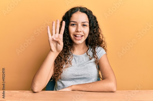 Teenager hispanic girl wearing casual clothes sitting on the table showing and pointing up with fingers number four while smiling confident and happy. © Krakenimages.com