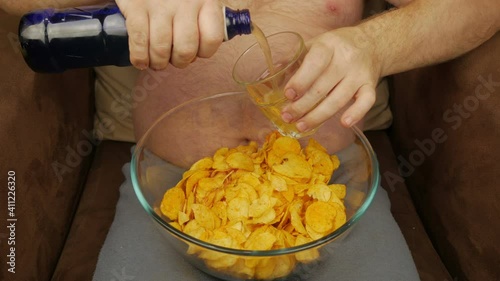 A Man With A Bare Belly Drinks Beer And Eats Chips