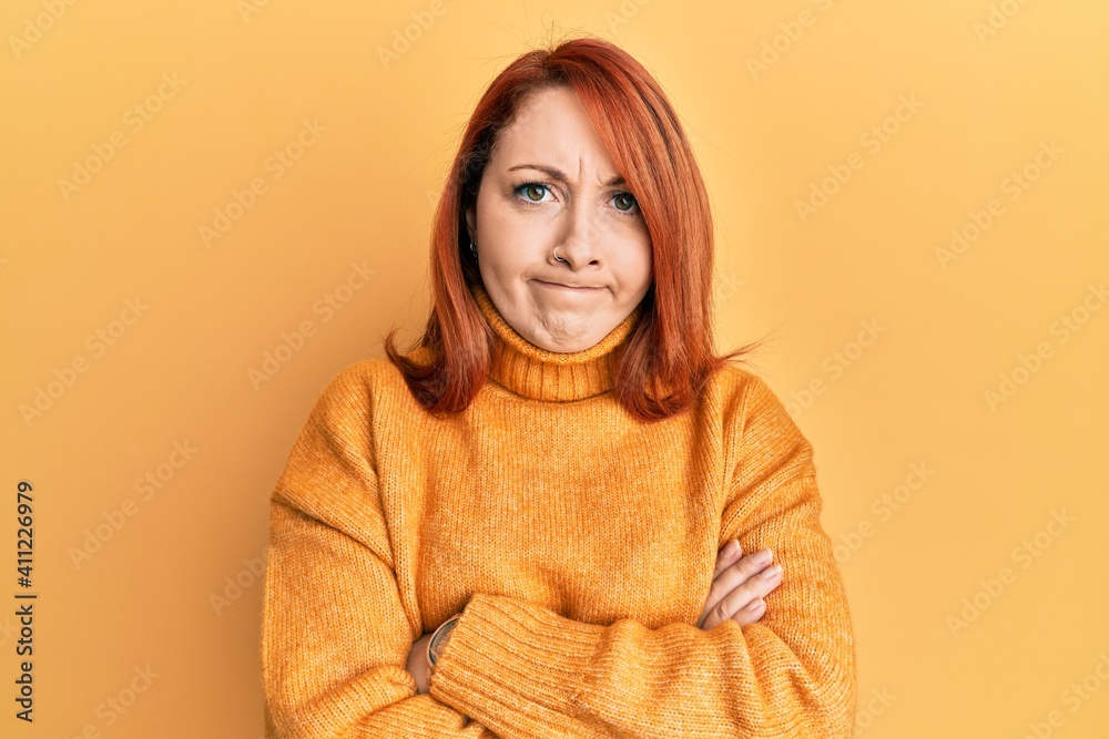 Beautiful redhead woman wearing casual winter sweater over yellow background skeptic and nervous, disapproving expression on face with crossed arms. negative person. Beautiful redhead woman wearing casual winter sweater over yellow background skeptic and nervous, disapproving expression on face with crossed arms. negative person.