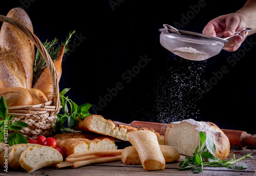 Fotografie Hand sifting flour on a bread in a wood table with variety of breads