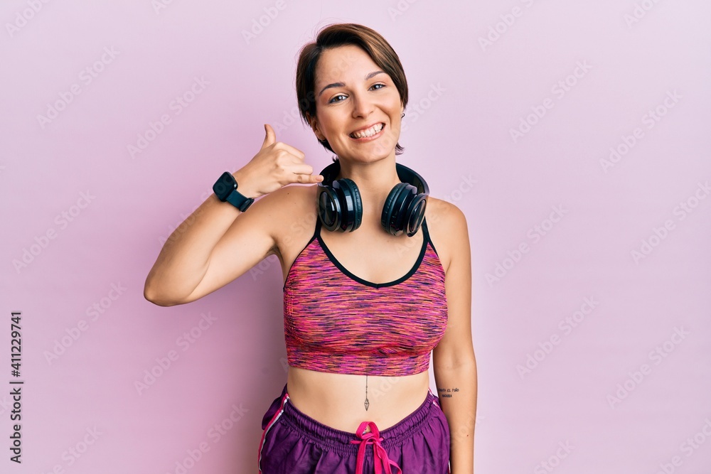 Obraz premium Young brunette woman with short hair wearing sportswear and headphones smiling doing phone gesture with hand and fingers like talking on the telephone. communicating concepts.