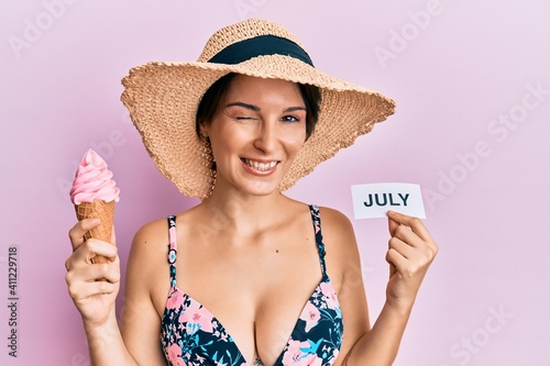 Young brunette woman with short hair holding ice cream and july paper winking looking at the camera with sexy expression, cheerful and happy face.