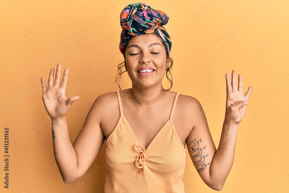 Young hispanic girl wearing hair turban over yellow background showing and pointing up with fingers number nine while smiling confident and happy. Young hispanic girl wearing hair turban over yellow background showing and pointing up with fingers number nine while smiling confident and happy.