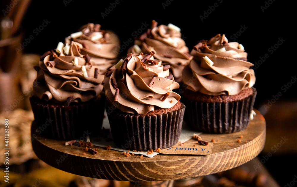 homemade tasty chocolate cupcakes with chocolate cream on wooden cake stand on rustic table. selective focus homemade tasty chocolate cupcakes with chocolate cream on wooden cake stand on rustic table. selective focus