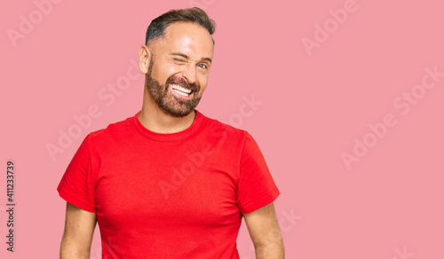 Handsome middle age man wearing casual red tshirt winking looking at the camera with sexy expression, cheerful and happy face.