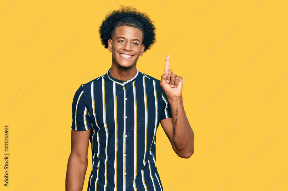 African american man with afro hair wearing casual clothes showing and pointing up with finger number one while smiling confident and happy. - obrazy, fototapety, plakaty 