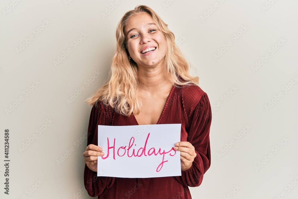 Young blonde girl holding holidays banner message smiling and laughing hard out loud because funny crazy joke. Young blonde girl holding holidays banner message smiling and laughing hard out loud because funny crazy joke.