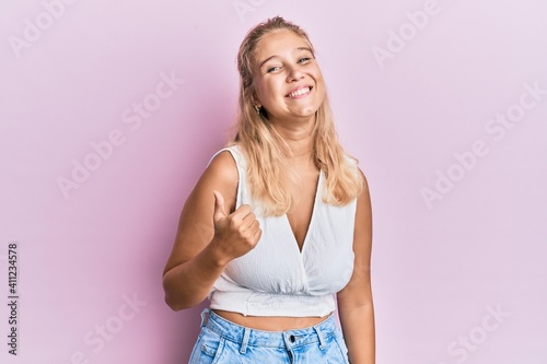 Young blonde girl wearing casual clothes doing happy thumbs up gesture with hand. approving expression looking at the camera showing success.