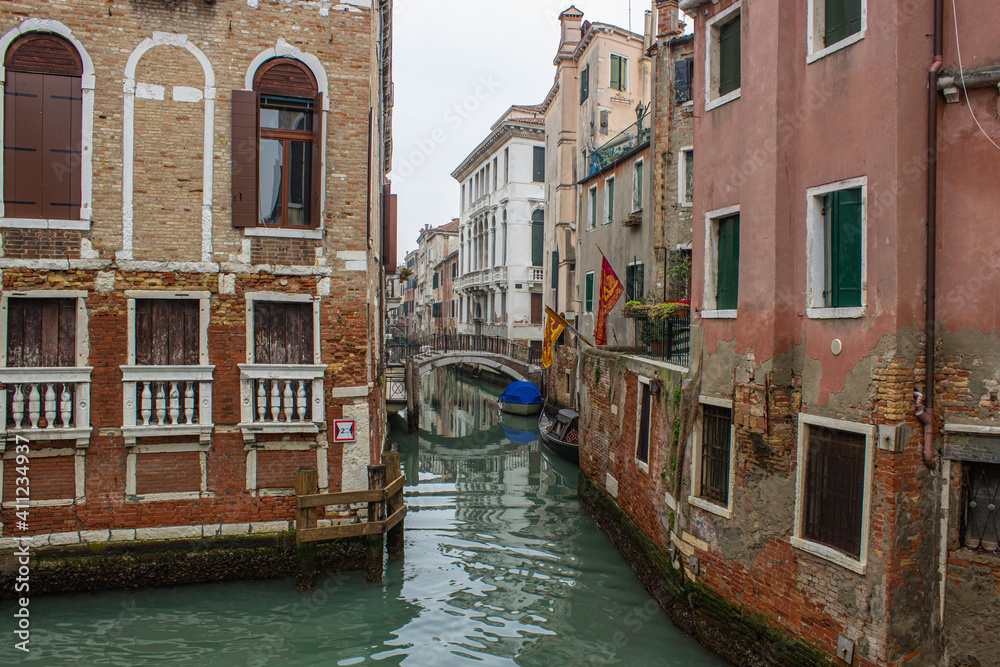 View of a small canal in Venice with old houses with Venetian flags. Gloomy winter day.