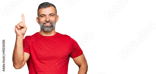 Middle age handsome man wearing casual clothes showing and pointing up with finger number one while smiling confident and happy.