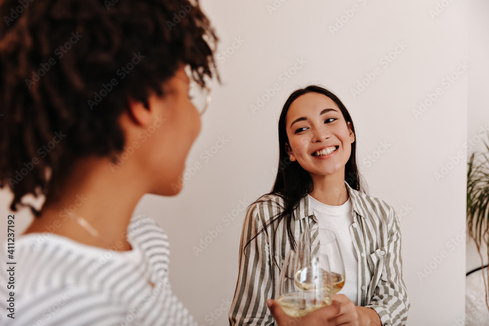 Pretty woman in shirt clink glasses of champagne with curly girl Pretty woman in shirt clink glasses of champagne with curly girl