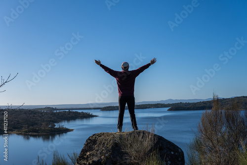 Photo of a young and attractive man on the top of a rock next to the sea with his arms open pointing to the sky. Sunny day of winter. © Irene Castro Moreno