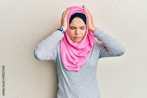 Young caucasian woman wearing traditional islamic hijab scarf suffering from headache desperate and stressed because pain and migraine. hands on head. © Krakenimages.com