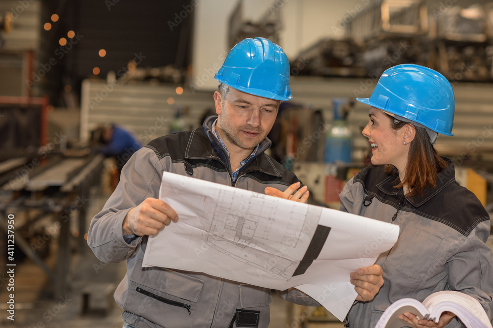 Two workers are having fun in the factory while they are reading Two workers are having fun in the factory while they are reading