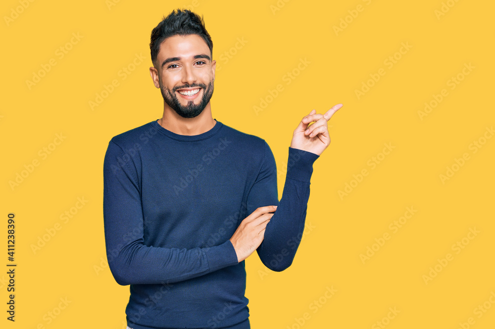 Young man with beard wearing casual blue winter sweater smiling happy pointing with hand and finger to the side Young man with beard wearing casual blue winter sweater smiling happy pointing with hand and finger to the side