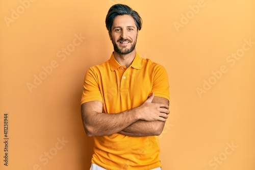 Young hispanic man wearing casual yellow t shirt happy face smiling with crossed arms looking at the camera. positive person.