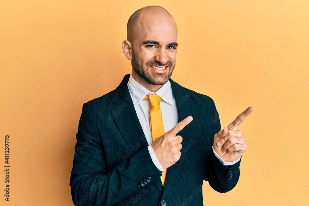 Young hispanic man wearing business suit and tie smiling and looking at the camera pointing with two hands and fingers to the side.