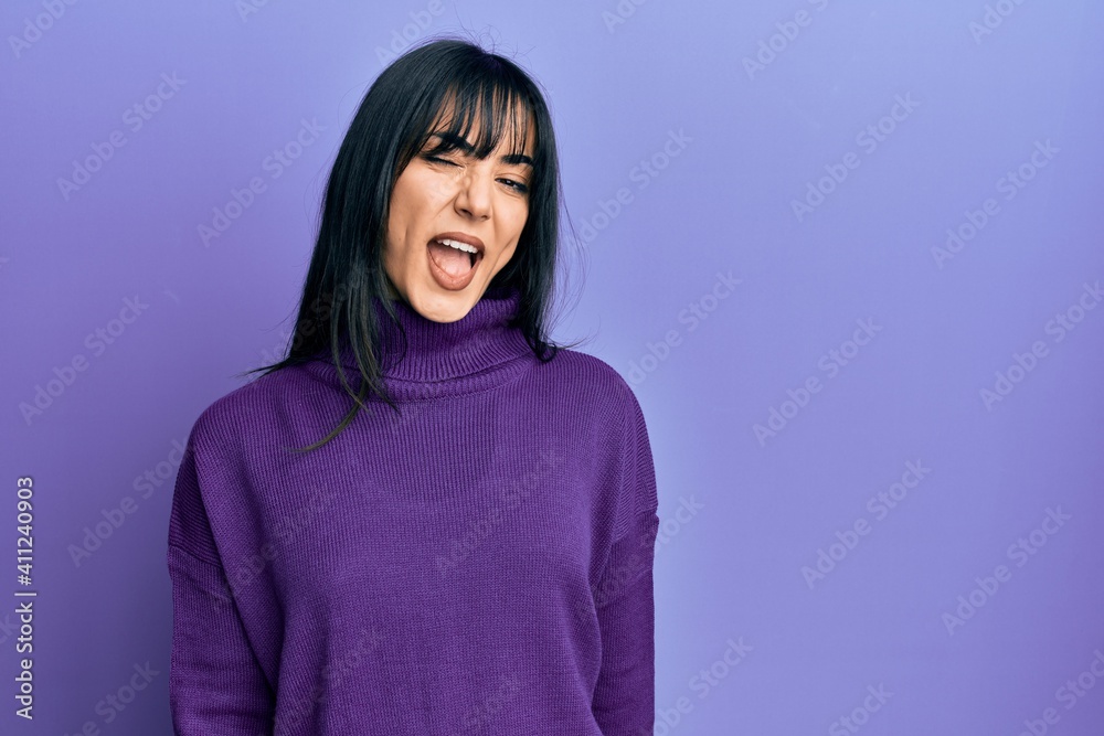 Young brunette woman with bangs wearing turtleneck sweater winking looking at the camera with sexy expression, cheerful and happy face. Young brunette woman with bangs wearing turtleneck sweater winking looking at the camera with sexy expression, cheerful and happy face.
