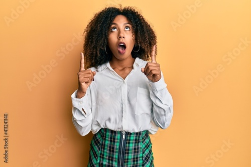 Canvas Print Beautiful african american woman with afro hair wearing scholar skirt amazed and surprised looking up and pointing with fingers and raised arms