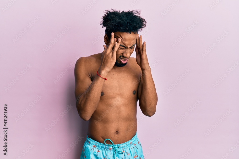 Fototapeta premium Young african american man with beard wearing swimsuit with hand on head for pain in head because stress. suffering migraine.