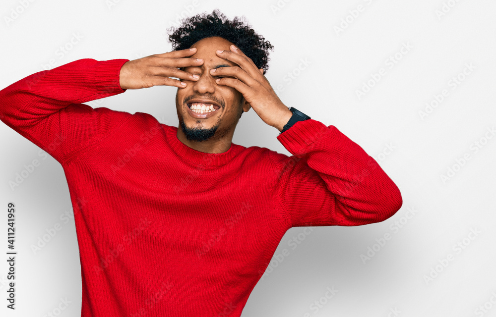 Young african american man with beard wearing casual winter sweater covering eyes with hands smiling cheerful and funny. blind concept. Young african american man with beard wearing casual winter sweater covering eyes with hands smiling cheerful and funny. blind concept.