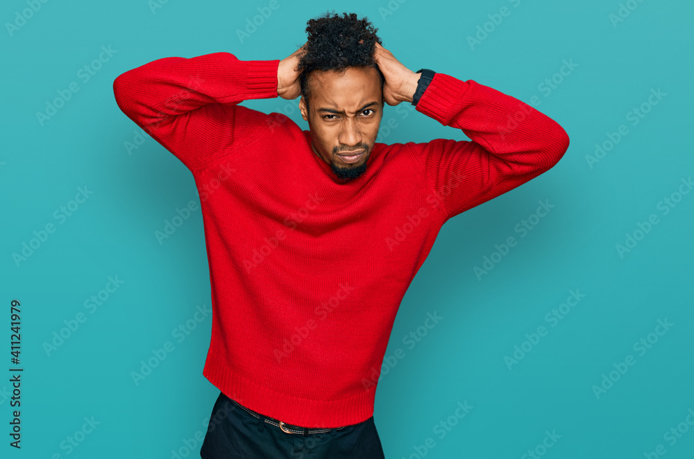Fototapeta premium Young african american man with beard wearing casual winter sweater crazy and scared with hands on head, afraid and surprised of shock with open mouth